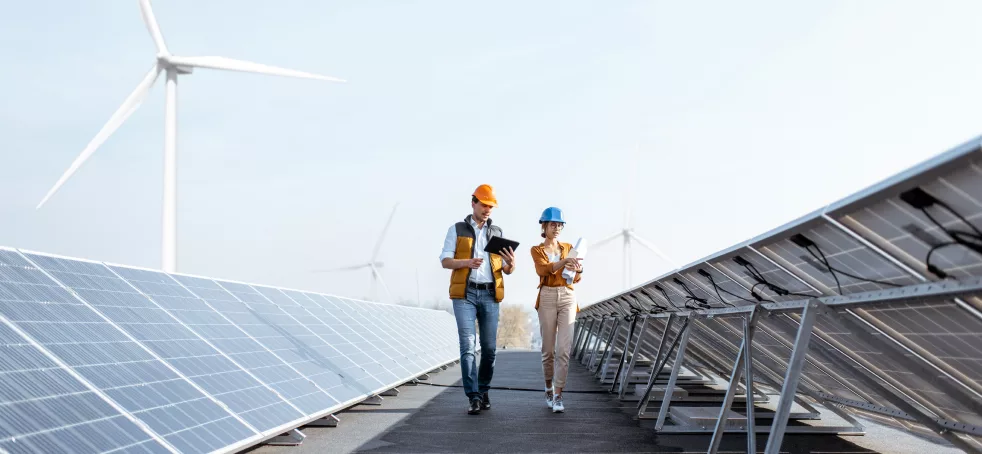 People discuss, energy collectors and windmills around them, representing sustainable energy initiatives